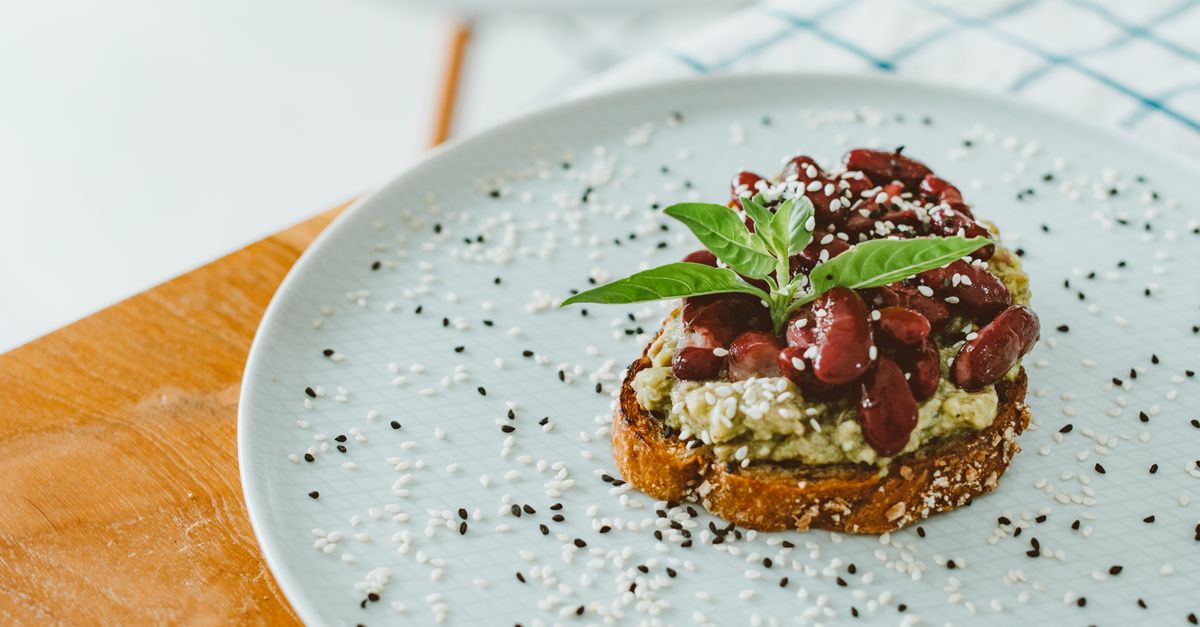 Appetizing toast topped with avocado, kidney beans, and sesame seeds on a plate.